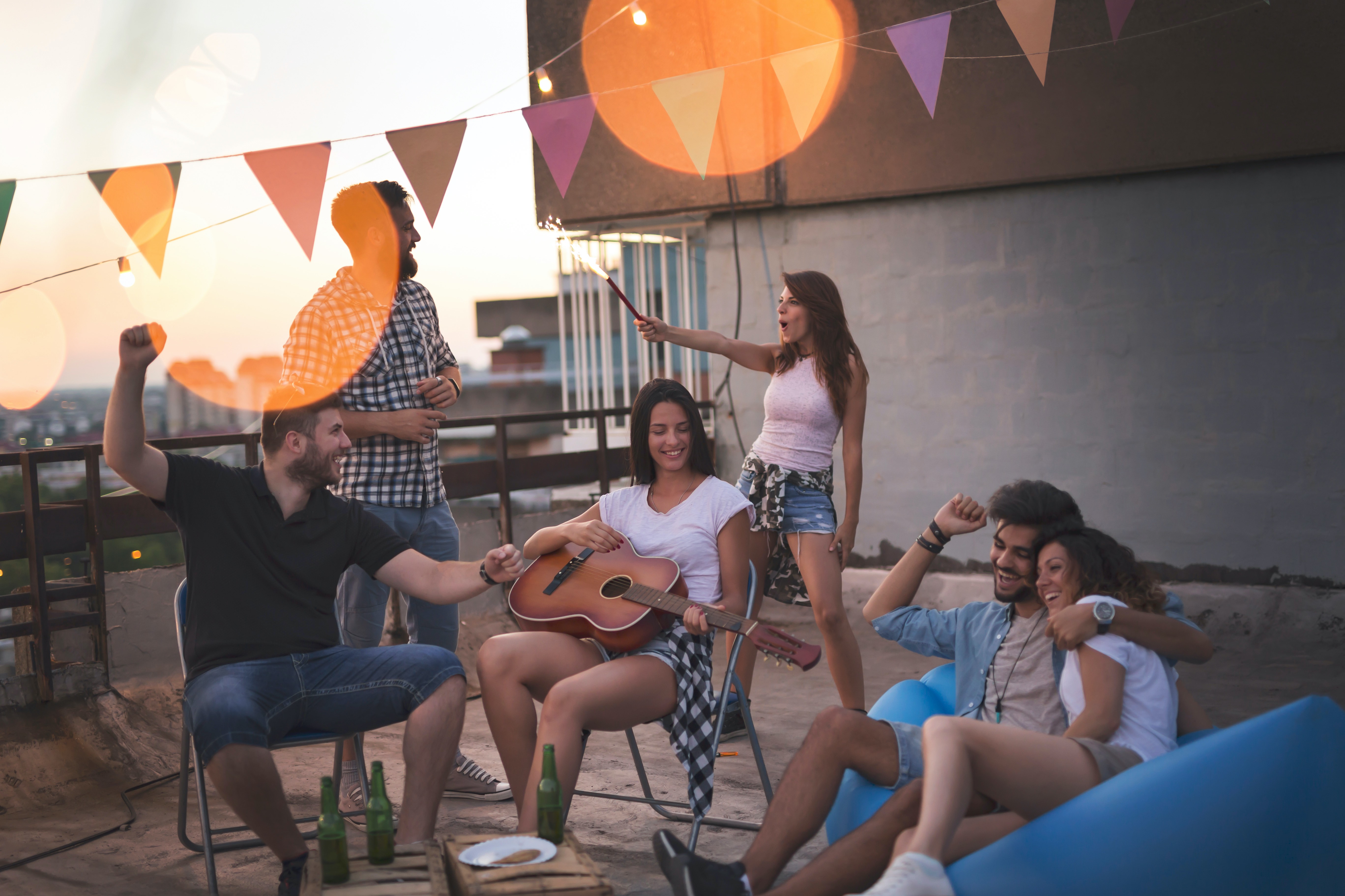 Young friends having fun at a rooftop party, playing the guitar, singing, dancing and chilling out. Focus on the girl playing the guitar